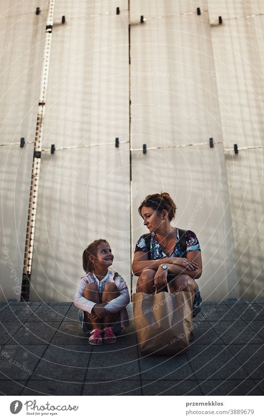 Mother and her little daughter resting in a public place outdoors after shopping in the evening child woman parent mother girl family sitting lighted backlit