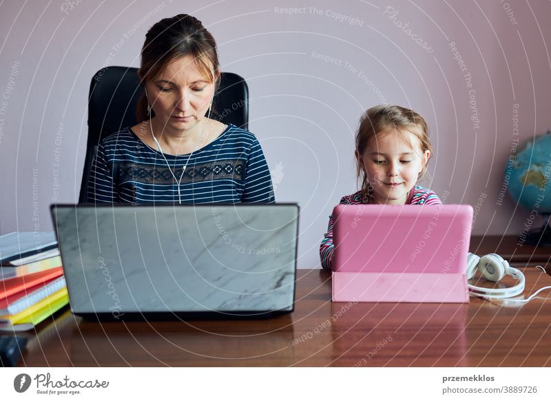 Woman mother working doing her job remotely during video chat call stream online course webinar on laptop from home while her daughter watching video on tablet