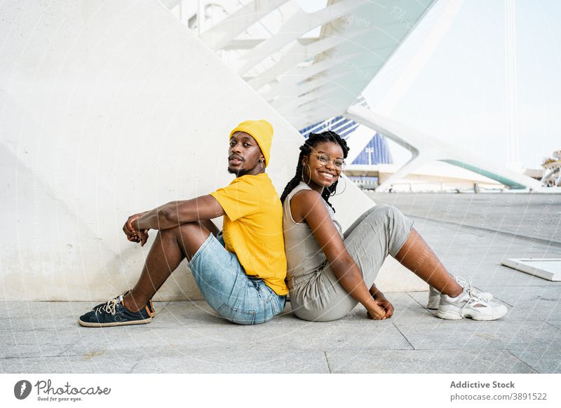 Black friends sitting back to back in city together street cool short hair appearance trendy young urban ethnic black african american rest style relax