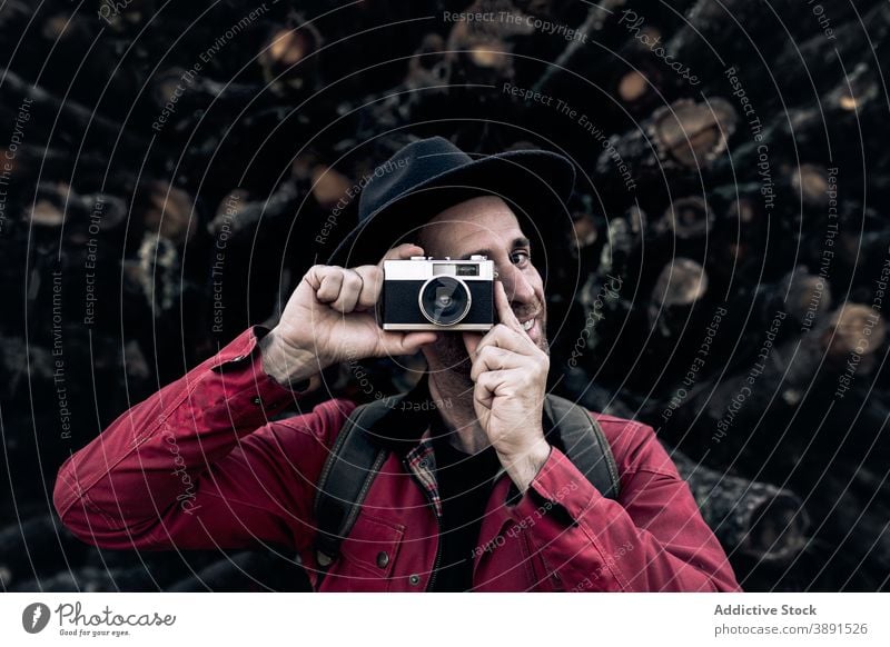 Smiling man with camera against tree logs photo camera vintage hipster wood lumber cheerful smile travel style pile hat photographer content adult retro