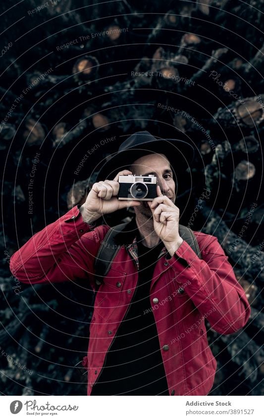 Smiling man with camera against tree logs photo camera vintage hipster wood lumber cheerful smile travel style pile hat photographer content adult retro