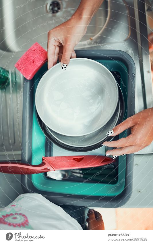 Teenager girl washing up the dishes pots and plates with help her younger sister in the outdoor kitchen during vacations on camping working together siblings