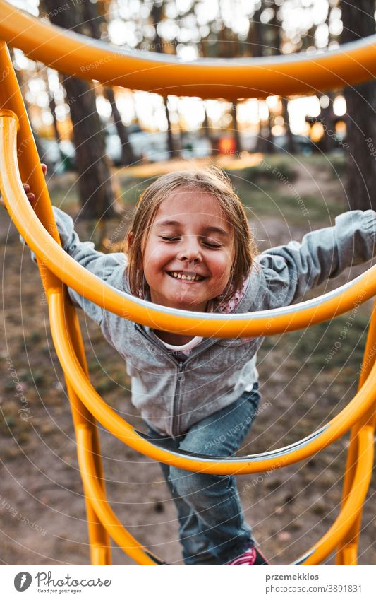 Playful happy girl preschooler playing on a playground climbing on monkey bars smiling with closed eyes positive joyful junior public place nursery outdoors