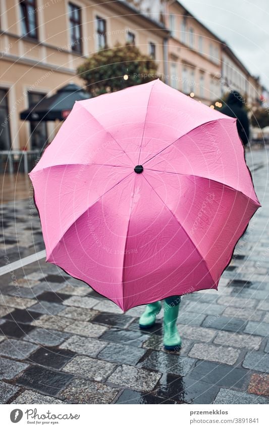 Child hiding behind big pink umbrella walking in a downtown on rainy gloomy autumn day raining outdoors little seasonal fall childhood beautiful weather outside