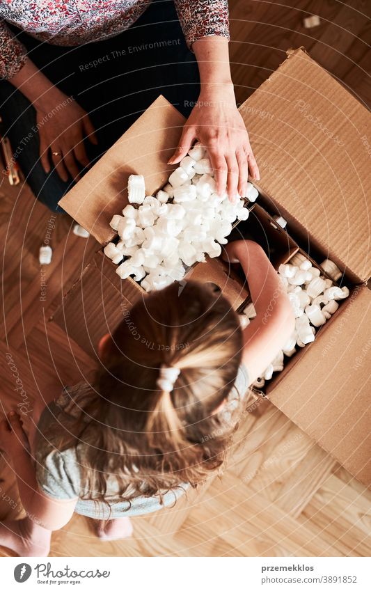 Woman unpacking a cardboard box parcel with help of her daughter view floor gift unboxing tape girl woman filler foam top open home wrapping opening shipping