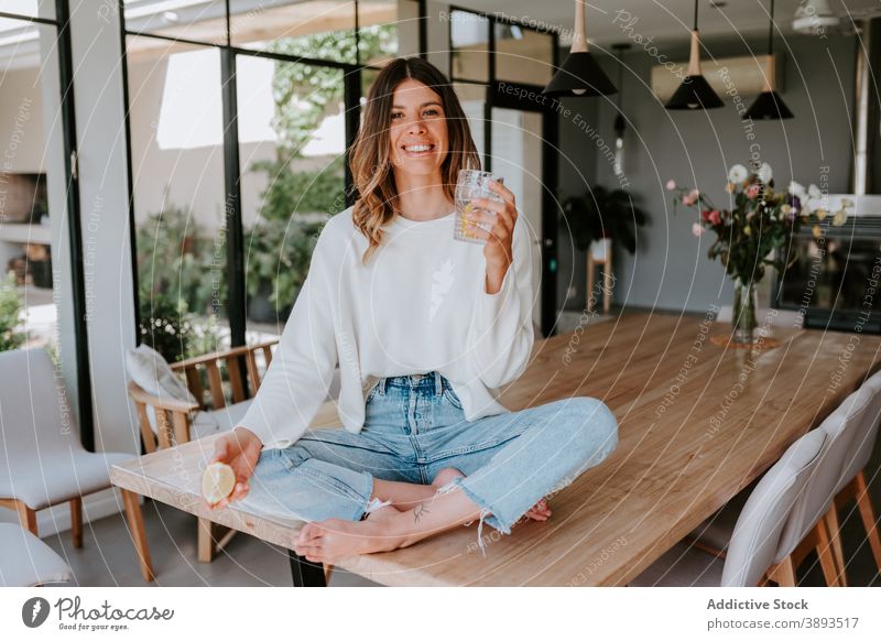 Smiling woman adding lemon juice in glass of water squeeze drink refreshment vitamin antioxidant beverage healthy female detox home natural citrus fruit organic