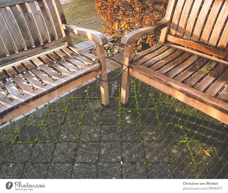 Neighborhoods | not optional...  Two wooden benches stand tied together on grey stone pavement with mossy joints. Light and shadow from the low sun. In the background a hedge with autumn colours