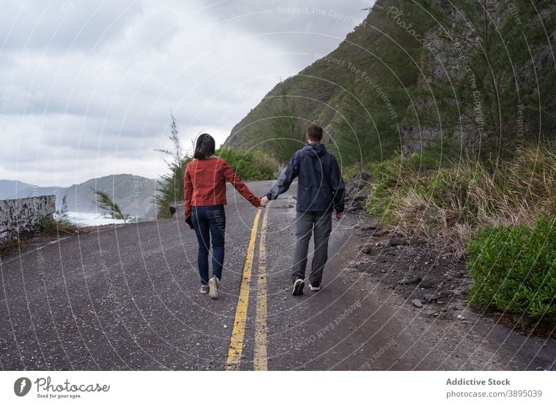 Anonymous couple walking on road near sea travel coast stormy ocean destroy overcast together asphalt coastline nature shore cloudy seashore seaside wave broken