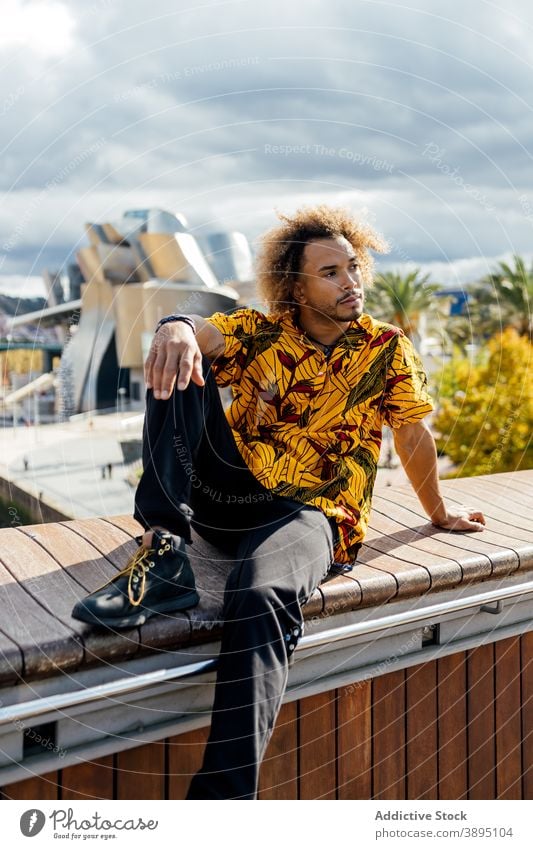 Confident trendy hipster man resting on street style informal fashion curly hair beard young modern colorful outfit guy african american black ethnic male