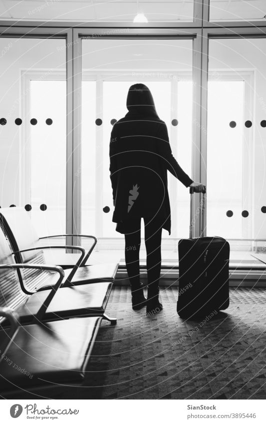 Young woman in the airport, looking through the window at planes travel b/w black white terminal flight airplane girl female luggage departure transportation