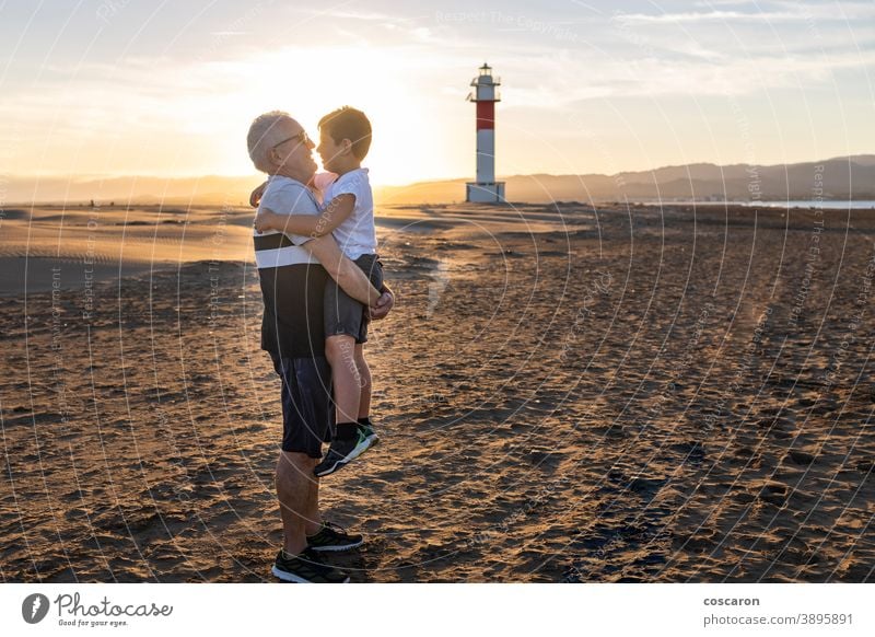 Grandfather and grandson hugging on a beach with a lighthouse in the background boy child childhood children coast dad day elderly family fangar far del fangar