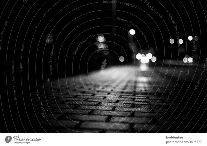 reflecting light of a street lamp on the paved sidewalk, in the background a bokeh of car lights and street lamps, focused on the foreground, frog's eye view