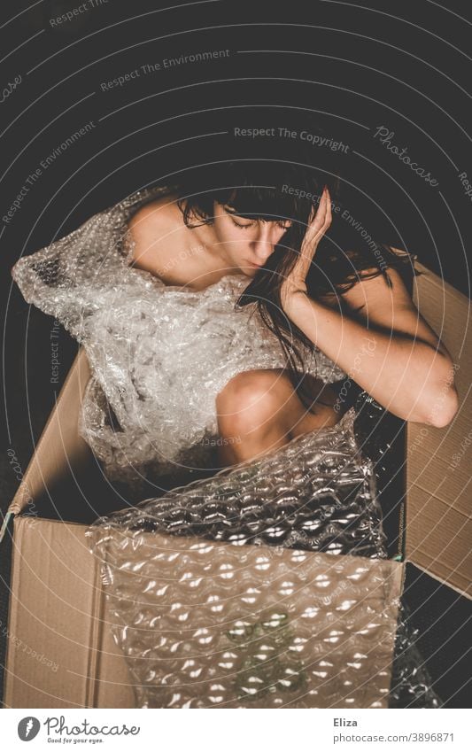 Woman sitting in a cardboard box between plastic packing material Cardboard Crate Human being Packaging Packaging material plastic foil Trash Plastic packaging