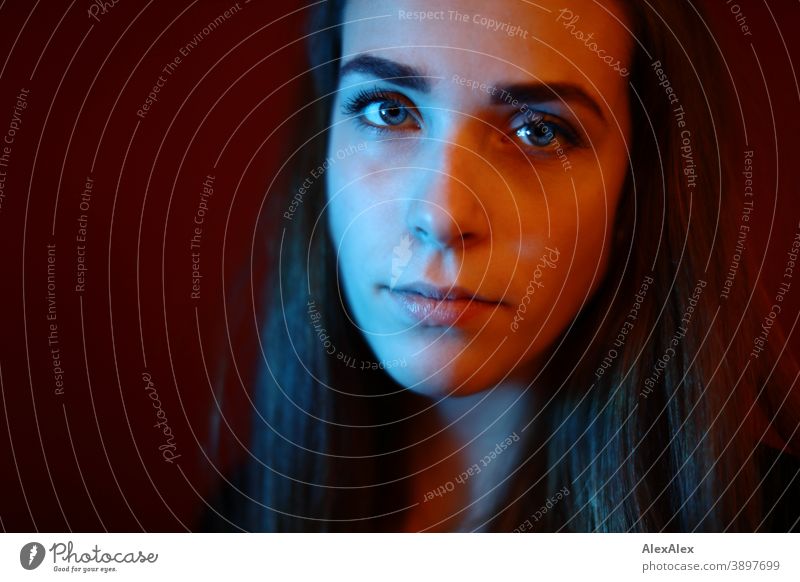 Portrait of a young woman in a room in front of a red wall with red and blue light Student daintily Facial expression empathy Looking into the camera