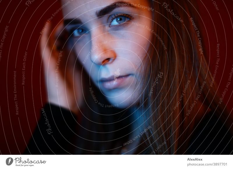 Portrait of a young woman in a room in front of a red wall with red and blue light Student daintily Facial expression empathy Looking into the camera