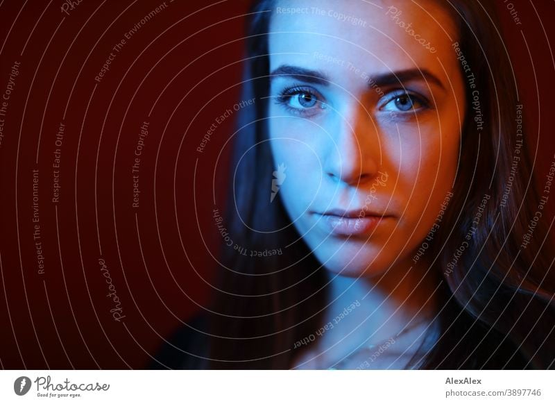 Portrait of a young woman in a room in front of a red wall with red and blue light Student daintily Facial expression empathy Looking into the camera