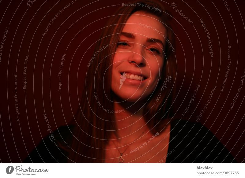 Portrait of a young woman in a room with red light Student kind daintily Jewellery Facial expression empathy Looking into the camera Copy Space left Close-up