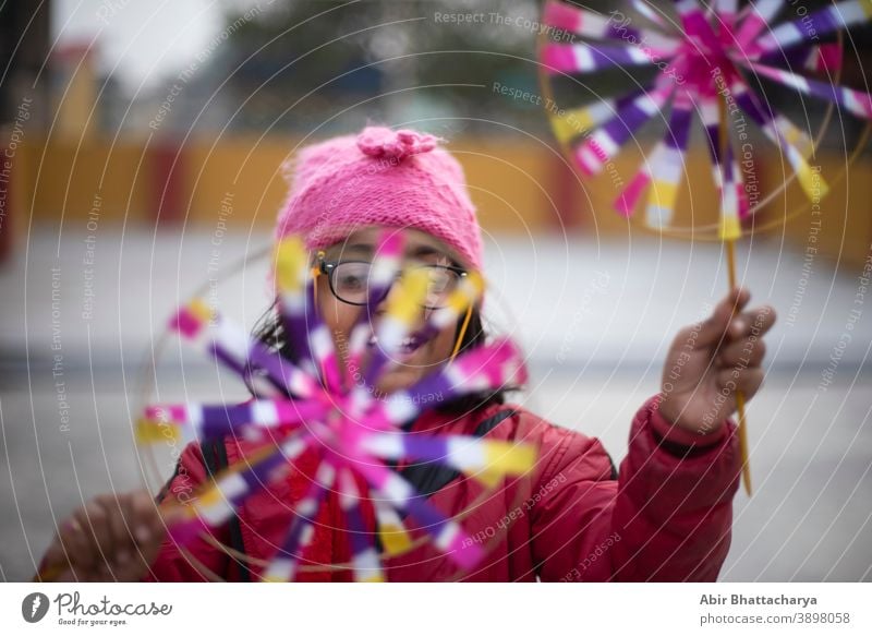 A cheerful Indian-Bengali brunette girl in a winter jacket and woolly hat enjoys the flywheel on the roof on a winter afternoon. Indian Lifestyle Asian