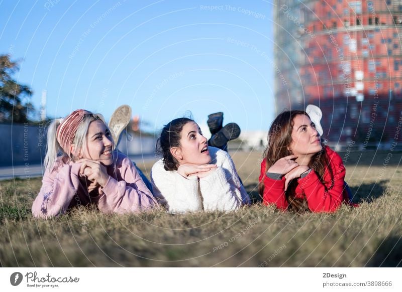 Three beautiful young women lie on the lawn, resting and daydreaming in the park on the green grass. happy lying woman three smiling friendship ground female