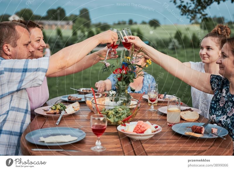 Family making toast during summer picnic outdoor dinner in a home garden feast having food man together woman child barbecue table eating gathering people