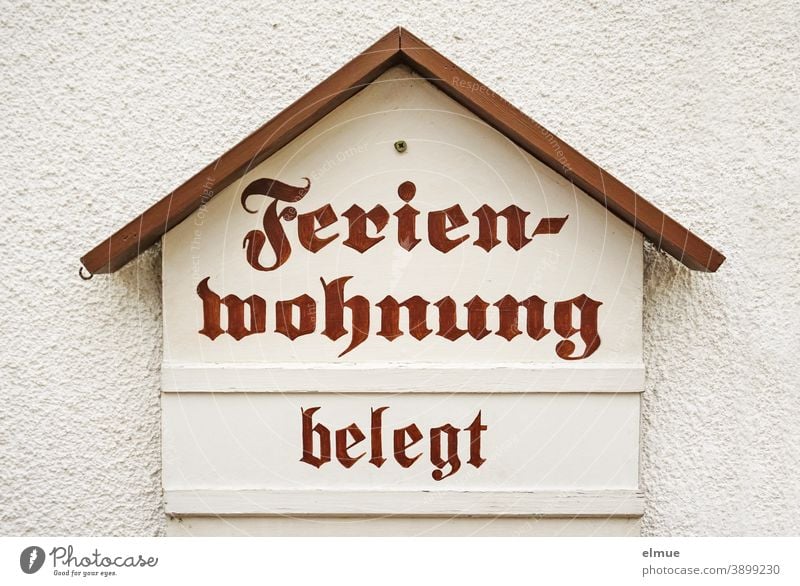 The wooden sign in the shape of a house on the plastered wall is clear: the holiday flat is occupied, nothing more is possible / ban on overnight stays / corona measure / lockdown