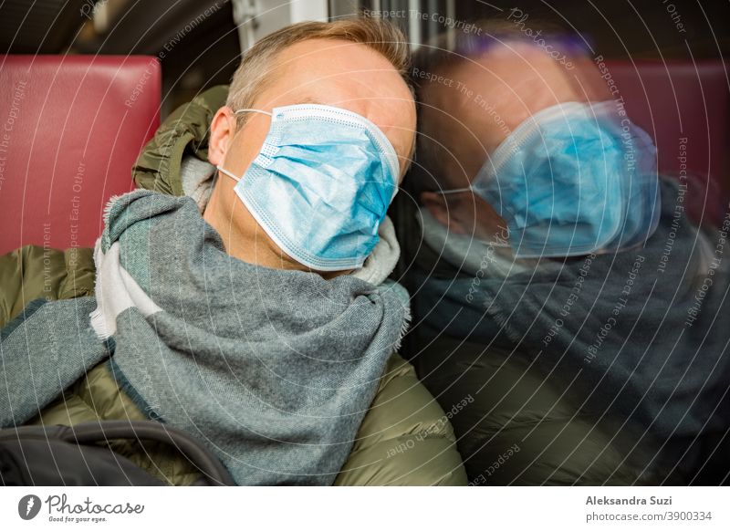 Traveling in public transport during the pandemic. Tired middle aged man wearing medical protective mask on his face sleeping in commuter train. city