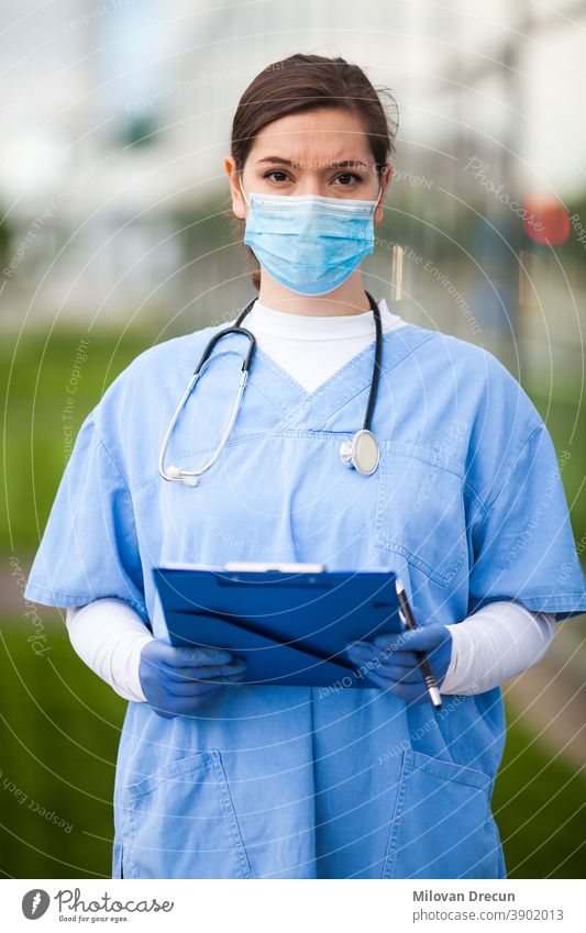 Portrait of very tired & exhausted female UK NHS doctor in front of hospital,blurry out of focus background, Coronavirus COVID-19 pandemic outbreak crisis,overworked medical staff working long shifts