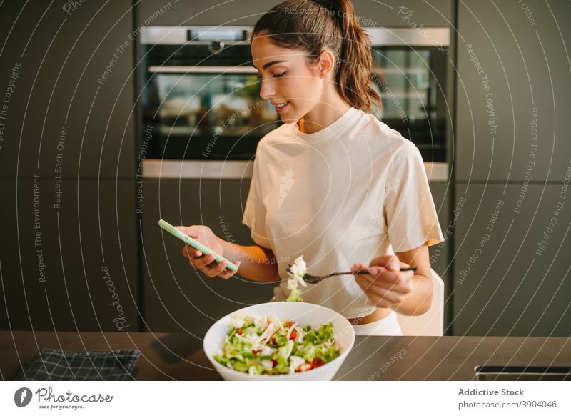 Woman having lunch and browsing smartphone at home woman eat salad vegetable healthy food kitchen social media female read news internet online surfing watch