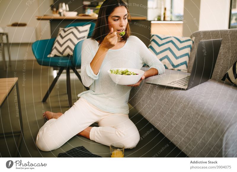 Young woman eating salad and watching video on laptop at home healthy young gadget food female casual lifestyle internet online using meal connection rest