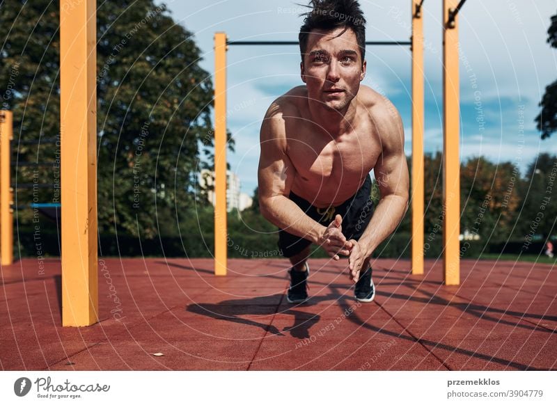 Young shirtless man bodybuilder doing clapping push-ups on a red rubber ground during his workout in a modern calisthenics park care caucasian health lifestyle