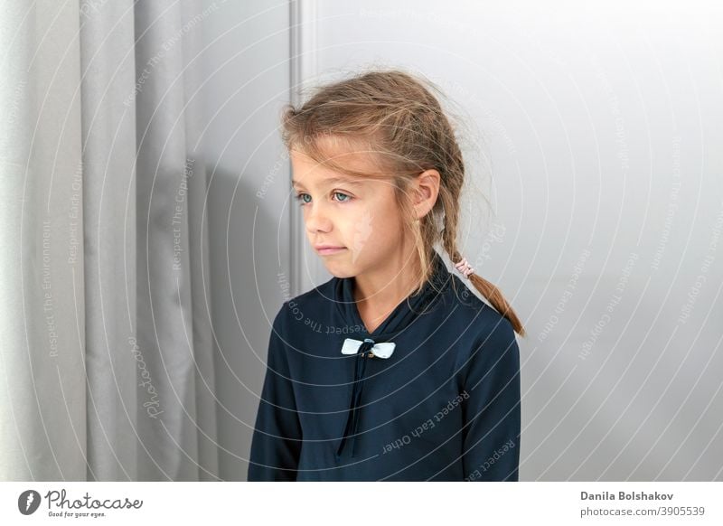 small girl looks into distance through brightly lit window behind curtain alone beauty bored calm casual caucasian child childhood concept coronavirus cute