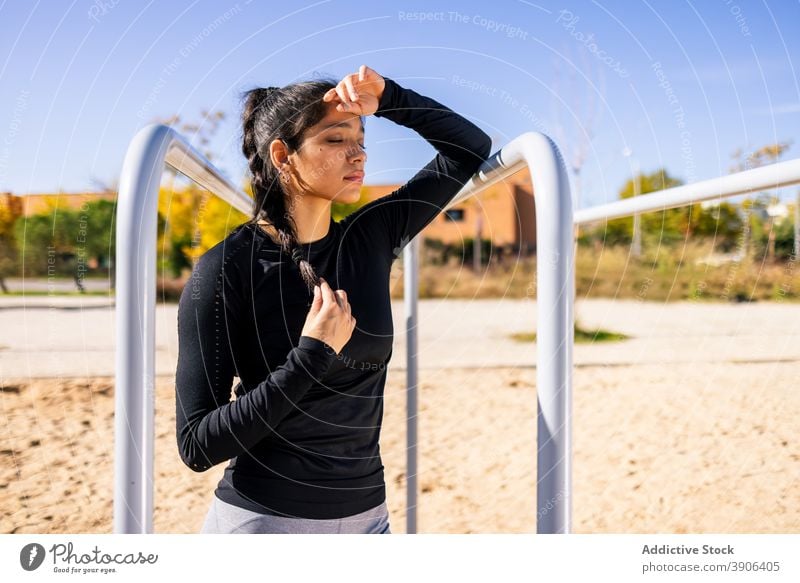 Tired sportswoman relaxing on sports ground tired exhausted training break weary sunny summer fatigue workout female ethnic athlete parallel bar wellbeing