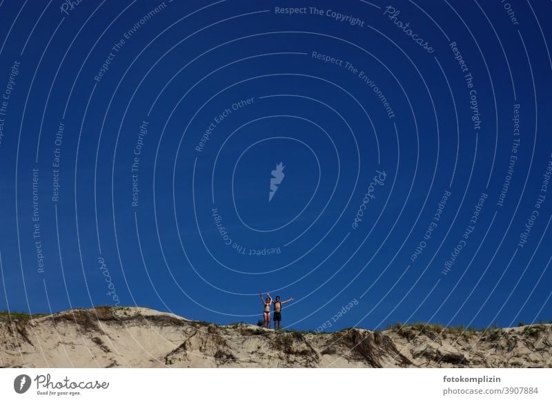 a couple / young woman and young man waving from a dune Ease Wave cheerful Summer vacation in common youthful breathe deeply Vacation mood holidays duene