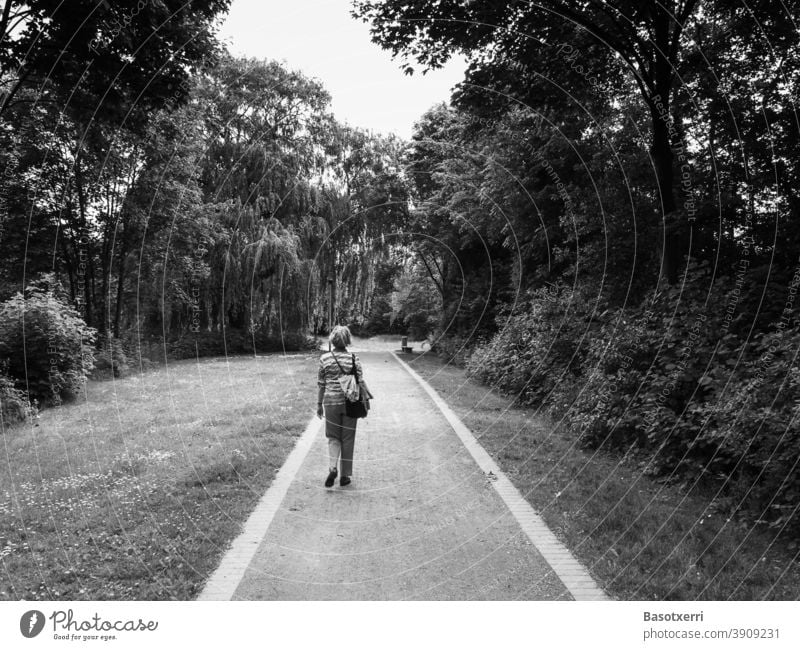 Older but modern lady on a path through a city park (black and white photo) Belm Osnabrück Lower Saxony Germany Park off gravel Gravel path Black & white photo