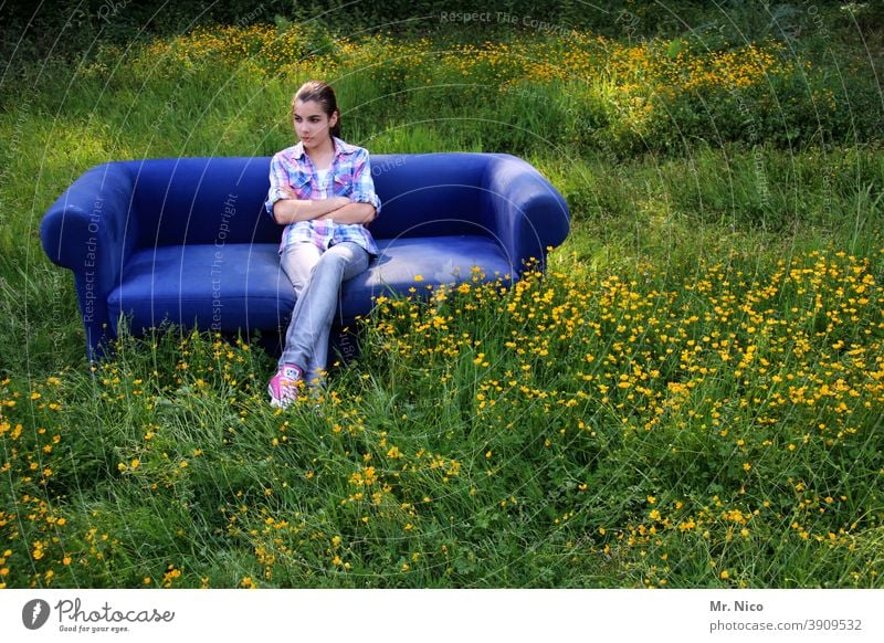 Young girl sits on a blue sofa which stands on a meadow Sit tranquillity relaxing relaxed portrait Happy Wait Grass Nature Environment Sofa Meadow naturally