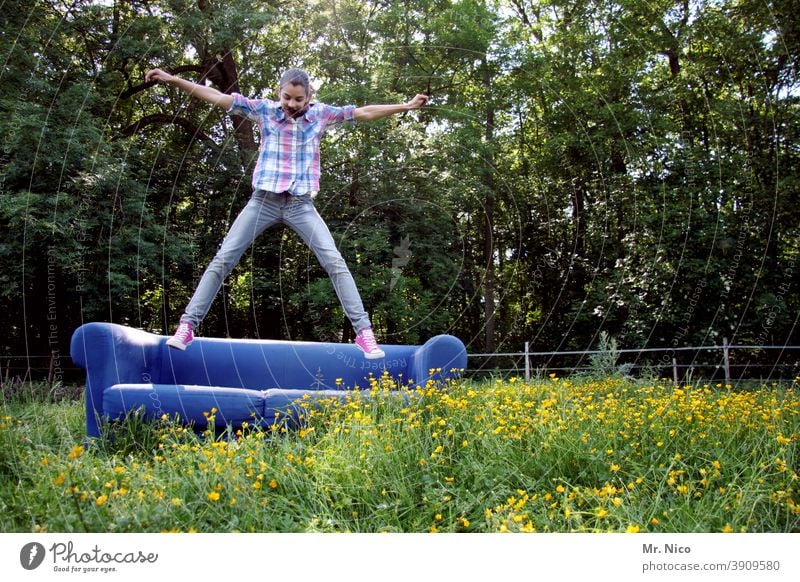 Young girl jumps on a blue sofa which stands on a green meadow Sofa Environment Nature Grass Meadow naturally Idyll Flower meadow Wild plant Summer Hop