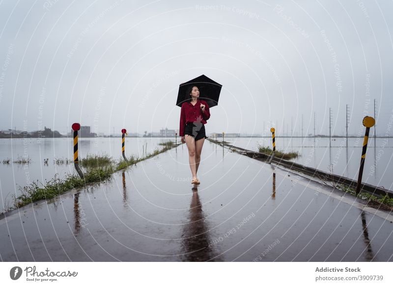 Woman walking along wet road on rainy day woman umbrella cloudy asphalt alone solitude stroll female yilan county taiwan empty overcast sky weather roadway