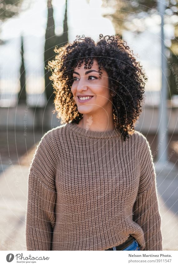 Beautiful female with curly hair in a park wearing a beige sweater and smiling. sunlight fashion portrait afro woman real woman human being ethnicity hairstyle