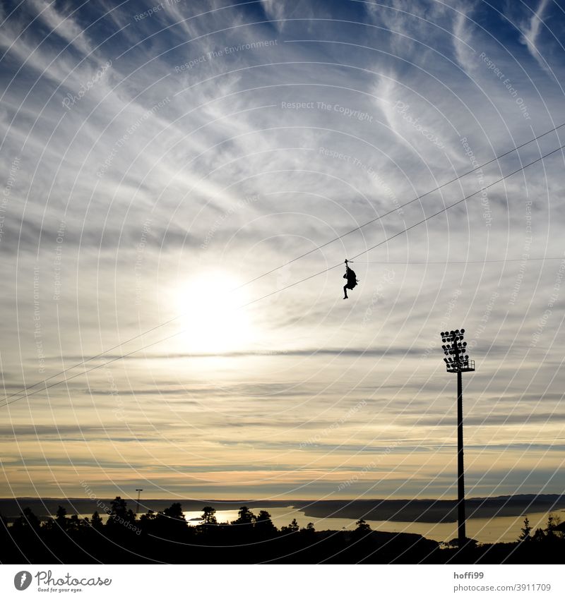 a man rides the Holmenkollen Zipline down from a mountain stump zipline Cable car Fjord Tourism Sunset Mountain Gondola Norway Clouds Water Nature Landscape Day