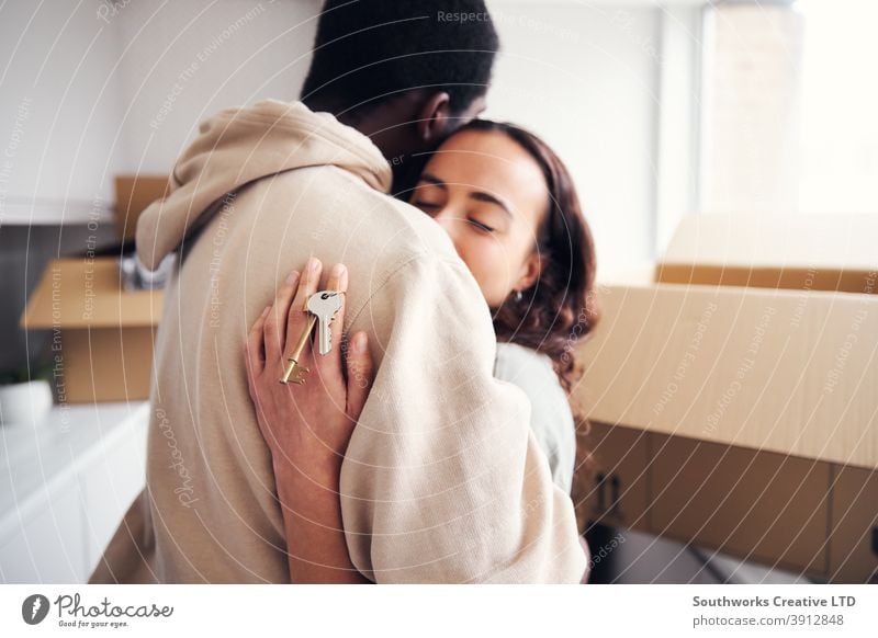 Young Couple With Keys To New Home Hugging As They Unpack Removal Boxes In Kitchen Together couple young couple house buying unpacking boxes keys holding home