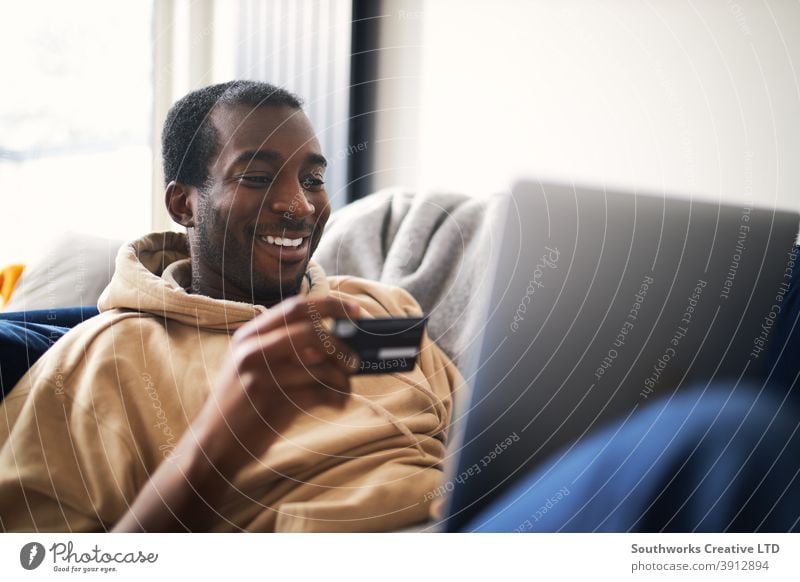 Young Man At Home Lying On Sofa With Laptop Using Credit Card To Shop Online man at home lying sofa lounge laptop computer credit card debit card pay day tech