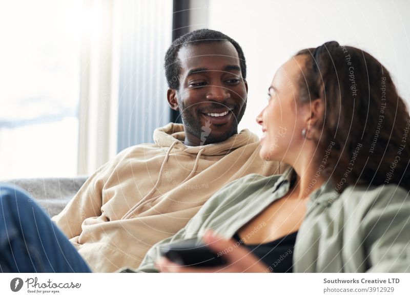 Young Smiling Couple Relaxing At Home Sitting On Sofa Checking Social Media On Mobile Phones Together couple young couple at home sitting sofa lounge mobile