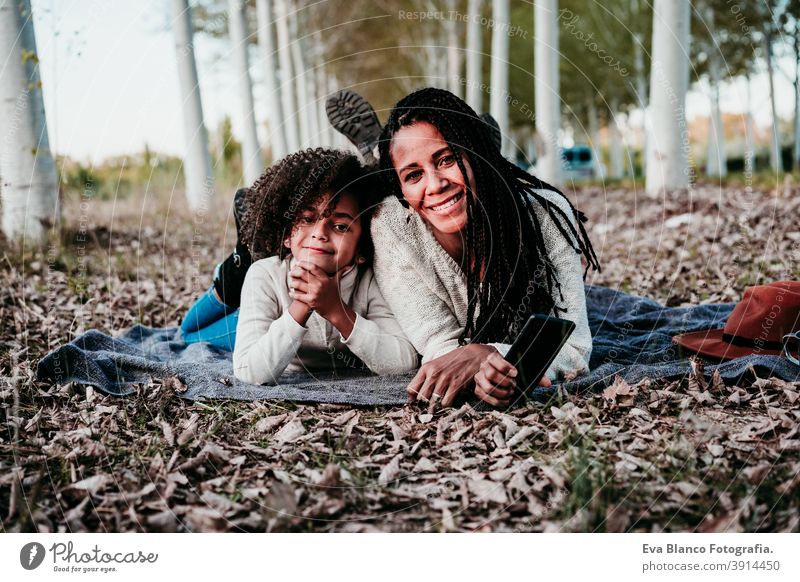 hispanic mother and afro kid girl outdoors lying on blanket. Autumn season. Family and love concept hug family woman daughter sunset nature together hat