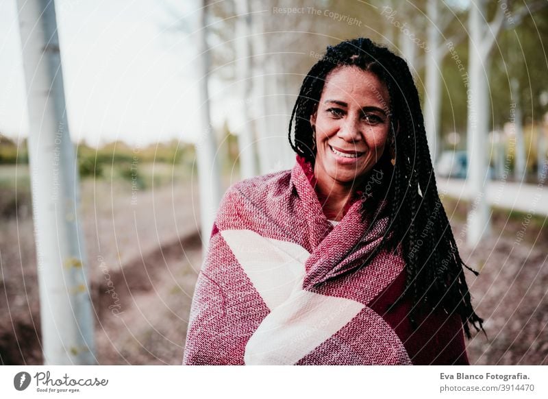 portrait of hispanic mid adult woman outdoors holding wrapped in blanket. Autumn season autumn afro woman latin sunset nature hat smile happy joy young