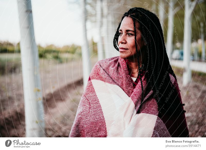 portrait of hispanic mid adult woman outdoors holding wrapped in blanket. Autumn season autumn afro woman latin sunset nature hat smile happy joy young