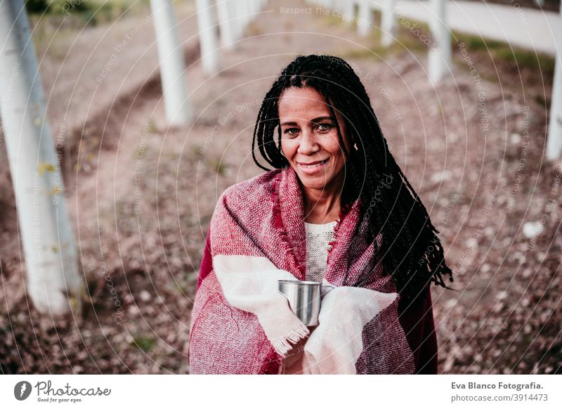 portrait of hispanic mid adult woman outdoors holding wrapped in blanket. Autumn season autumn afro woman latin sunset nature hat smile happy joy young