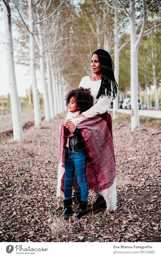 hispanic mother and afro kid girl outdoors hugging at sunset wrapped in blanket. Autumn season. Family and love concept family woman daughter nature together