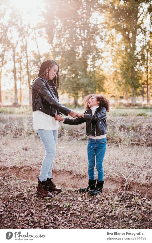 hispanic mother and afro kid girl outdoors hugging at sunset during golden hour. Autumn season. Family and love concept family woman daughter nature together