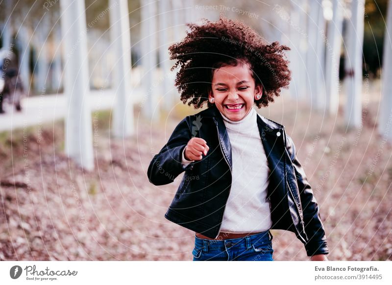 portrait of cute afro kid girl running at sunset during golden hour, autumn season, beautiful trees background fun nature outdoors hat brown leaves