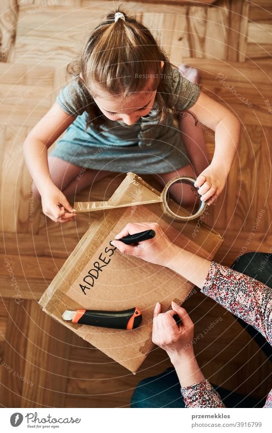 Woman writing an address on a cardboard box parcel preparing to send view floor gift unboxing tape girl daughter woman filler foam pack top open unpacking home